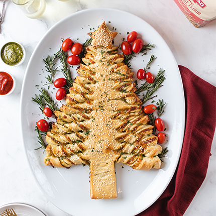 pesto pull apart bread in the shape of a christmas tree, on a plate with fresh herbs and cranberries